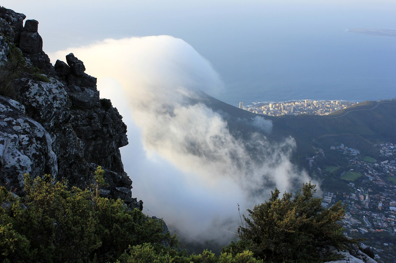 Vue depuis une montagne, avec des nuages descendant vers une ville côtière et l'océan en arrière-plan.