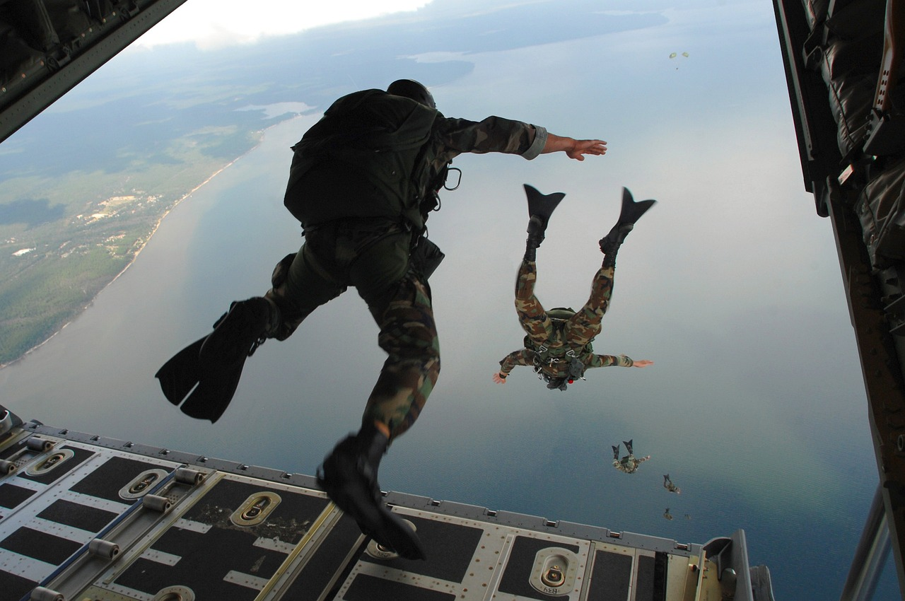 Soldats des forces spéciales sautant en parachute depuis un avion au-dessus de la mer, en tenue de camouflage et équipement complet.