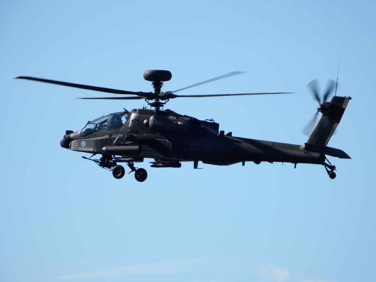 Hélicoptère Apache en vol, équipé pour les missions de combat et de soutien aérien, avec un ciel bleu en arrière-plan.