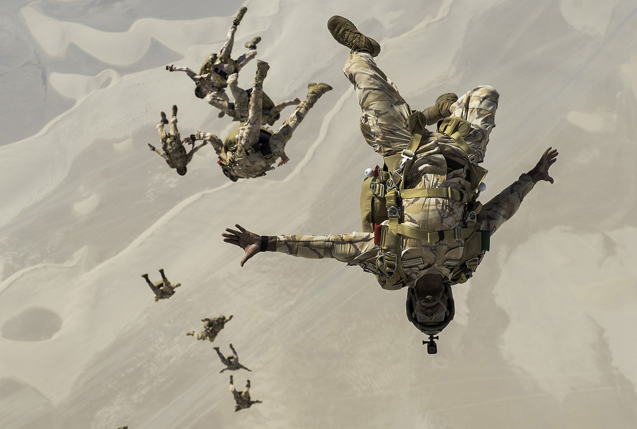 Soldats des forces spéciales effectuant un saut en parachute au-dessus d'un désert, en formation et en tenue de camouflage.