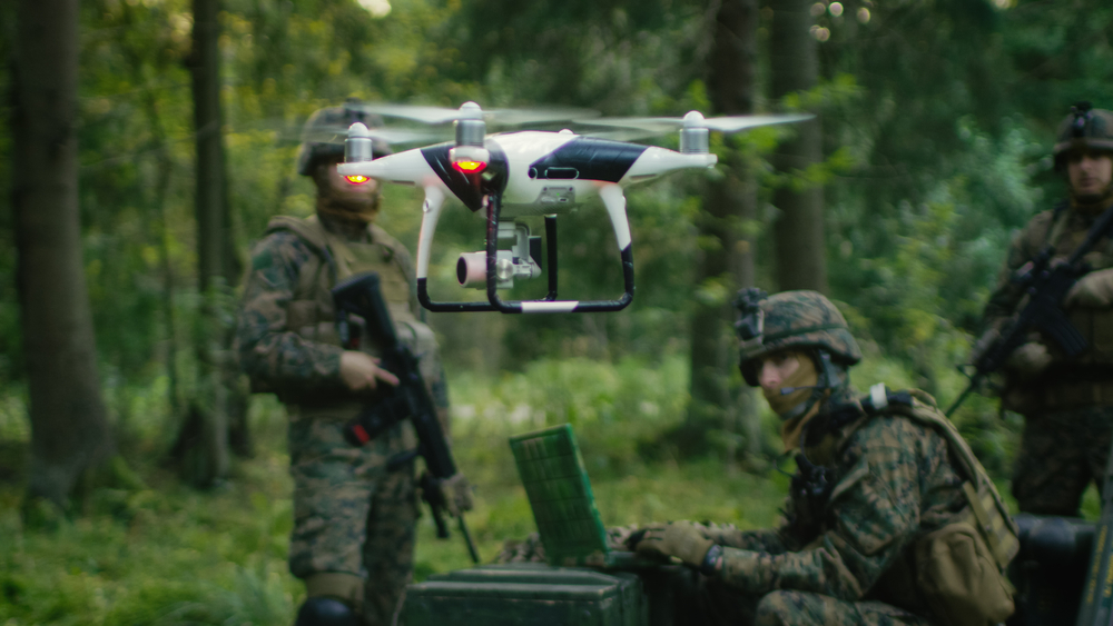 Drone militaire en vol avec des soldats en arrière-plan, en pleine opération de surveillance dans une forêt.
