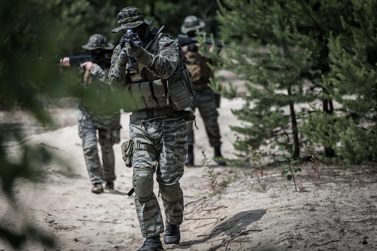 Un groupe de soldats avance prudemment dans une zone boisée, en formation tactique.