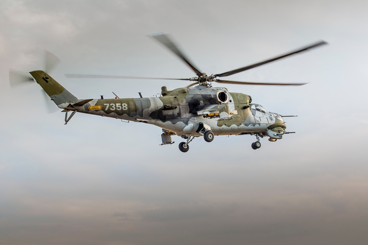 Hélicoptère militaire camouflé en vol avec ses pales en mouvement.