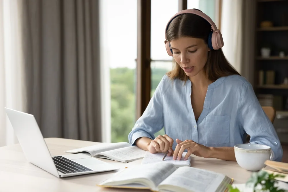Candidate révisant l'anglais pour un concours avec casque audio, ordinateur et manuels d'étude sur son bureau.
