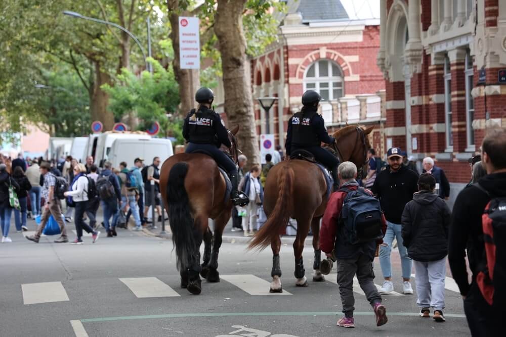Deux policières à cheval de dos dans une rue animée.