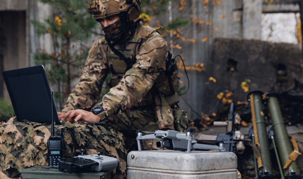 Un soldat en tenue de camouflage travaillant sur un ordinateur portable posé sur une caisse en métal