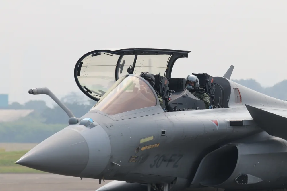 Aviateur en uniforme de l'Armée de l'Air et de l'Espace devant un avion militaire.