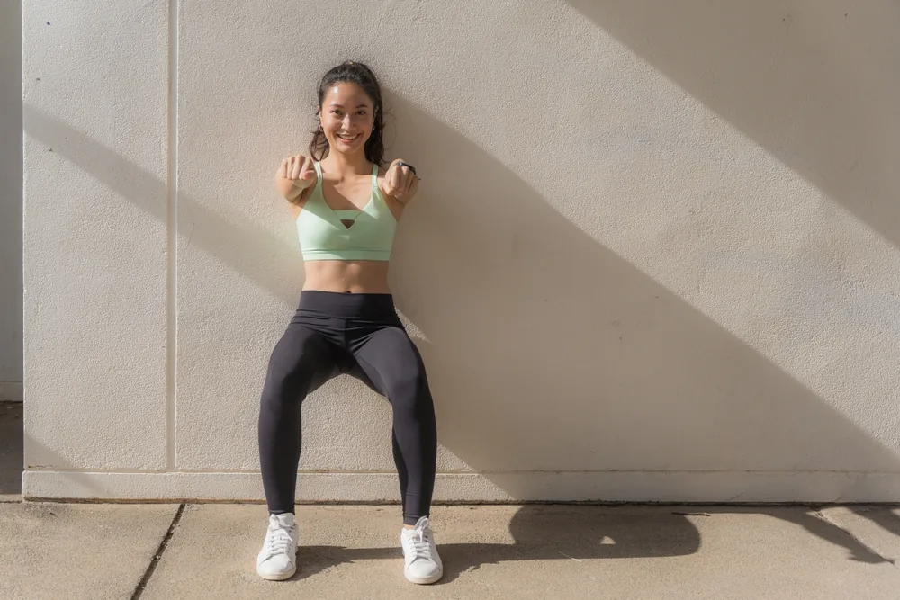 Sportif dos au mur en position chaise, cuisses parallèles au sol, lors d'un exercice de test Killy.