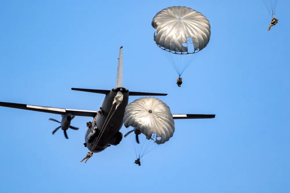 Soldats en formation parachutiste effectuant un saut en tandem depuis un avion militaire.