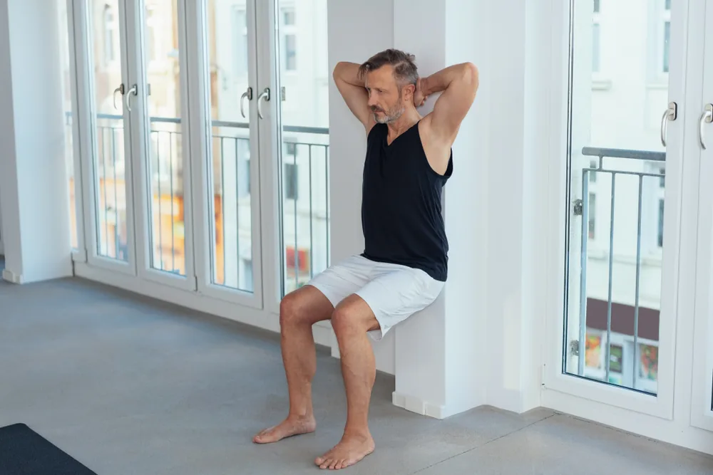 Sportif en tenue militaire tenant la position chaise contre un mur, genoux fléchis à 90° lors d'un test Killy.