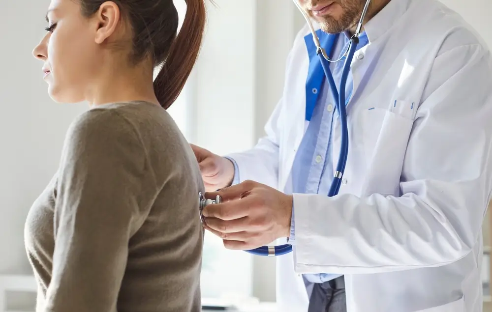 Médecin en blouse blanche auscultant une patiente avec un stéthoscope