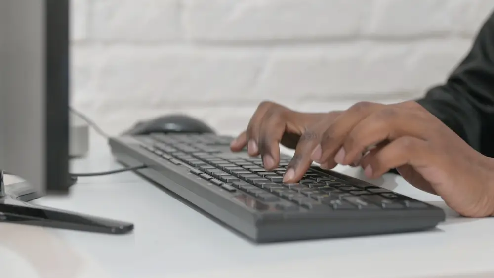 Manos escribiendo en el teclado de un ordenador de sobremesa, sobre una mesa despejada
