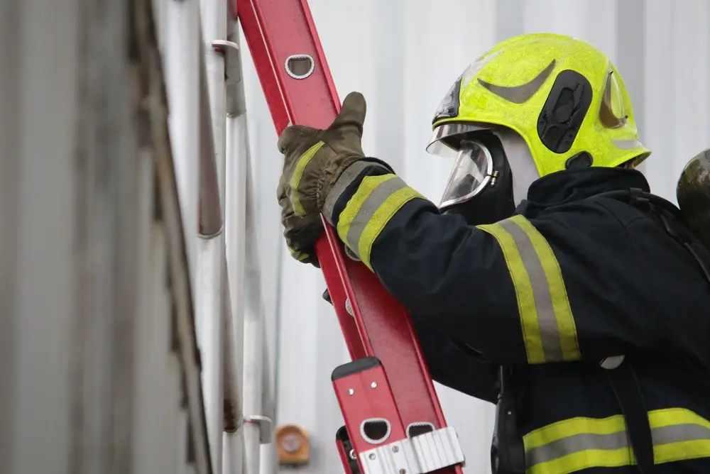 Sapeur-pompier en tenue de protection et casque jaune gravissant les échelons d'une échelle métallique