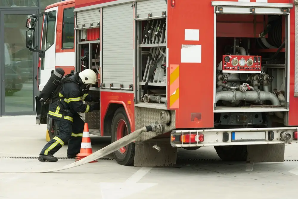 Sapeur-pompier en tenue d'intervention avec appareil respiratoire isolant manipulant une lance à l'arrière d'un camion-citerne rouge