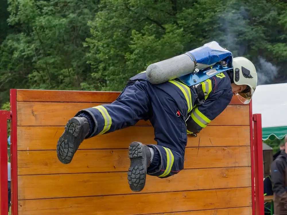 Candidat sapeur-pompier franchissant un obstacle en tenue d'intervention complète avec appareil respiratoire isolant (ARI)
